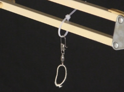 The tie strap around one arm of the desk lamp, with the fishing swivel hanging from the tie strap and a loop of string hanging from the swivel.